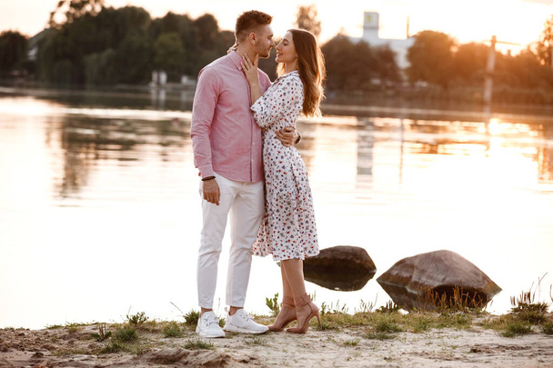 Szerető pár nézik egymást a tavon naplementekor. Gyönyörű fiatal szerelmesek, akik a tó partján sétálnak napnyugtakor az erős fényben. másolás helye. - Fotó, kép