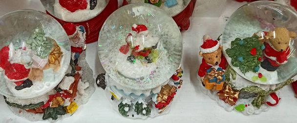 Kerstmannen in glazen ballen worden in de winkel verkocht. Kerstglazen sneeuwbal met de kerstman. Symbolisch cadeau voor Kerstmis. Een glazen kerstbal. Nieuwjaarsstemming. Speelgoedbal met sneeuw en kerstman - Foto, afbeelding