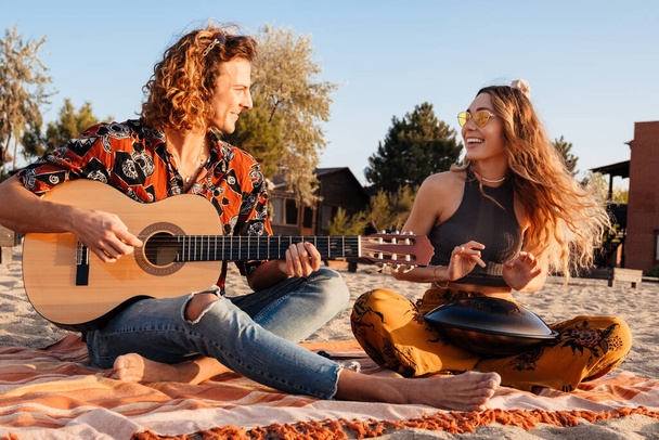 Image of happy positive young loving couple playing music on guitar and drum at the beach - Foto, Bild