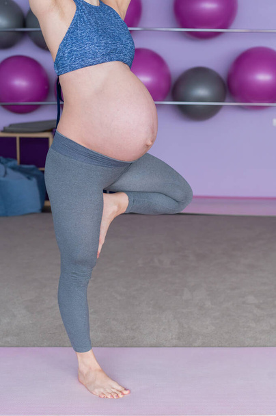 Cropped view of unrecognizable pregnant woman in yoga class. Future mother faceless with a bare tummy is engaged in fitness. Tree pose. - Foto, Imagem