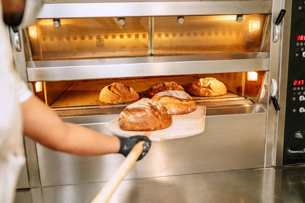 селективное внимание пекаря-латиноамериканца кладет хлеб в духовку в перчатках и маске в связи с пандемией коронавируса 2020 года covid19 - Фото, изображение