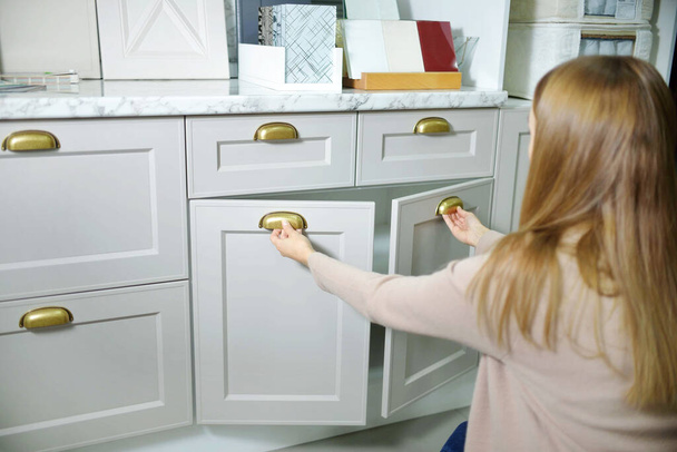 Концепция улучшения дома. молодая девушка дизайнер открывает ящик кухонного шкафа в салоне магазина - Фото, изображение
