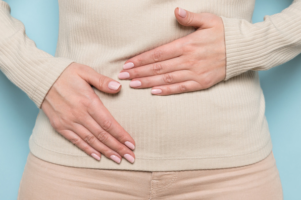 Close up of upset woman hold belly suffer from abdomen ache, female feel pain hurt in stomach abdominal gastritis, pancreatitis, food poisoning, appendicitis symptom, standing over blue wall. - Photo, Image