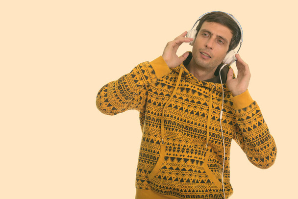 Στιγμιότυπο του νεαρού όμορφου άνδρα που ακούει μουσική ενώ κρατάει ακουστικά και σκέφτεται - Φωτογραφία, εικόνα
