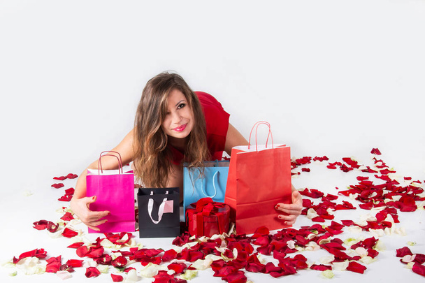 mujer con bolsas de compras de papel de regalo se ríe entre pétalos de rosa roja sobre fondo blanco. Regalos de San Valentín. compras para San Valentín... - Foto, imagen