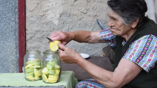 Vegyes fajú idős nő vágott friss cukkini szeletek belsejében üvegedények házi konzerválás - Felvétel, videó