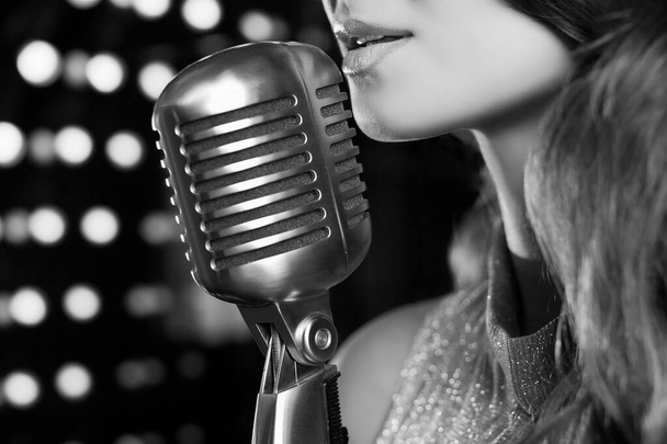 Close-up portrait of gorgeous singer woman in elegant dress with retro microphone on restaurant stage spotlights background. - Foto, afbeelding