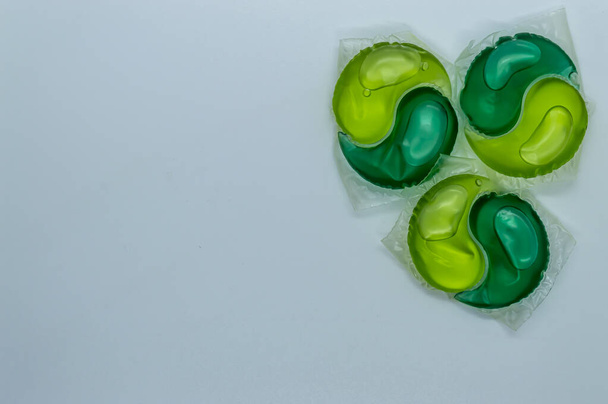 cápsulas para lavar con gel verde y amarillo sobre un espacio de copia de fondo blanco - Foto, imagen