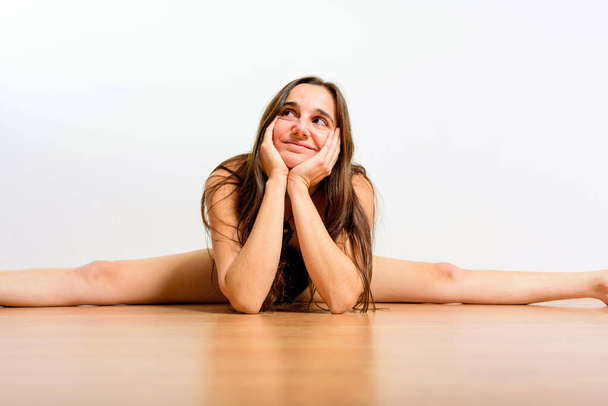 Jovem ginasta feminina descansa no chão com um rosto sonhador enquanto pratica uma divisão. - Foto, Imagem