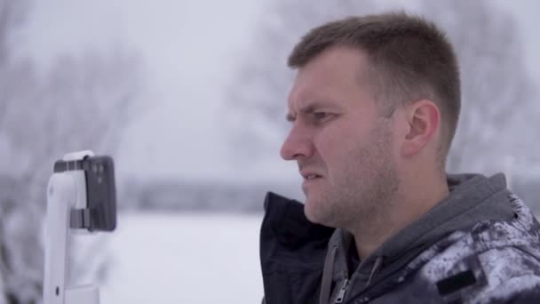 Um blogueiro masculino configura um telefone para uma transmissão ao vivo com assinantes durante uma viagem ao inverno na Rússia - Filmagem, Vídeo