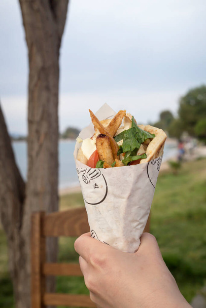 Famous, traditional Greek snacks grilled soufflaki in a womans hand, close-up on the sea background. - Photo, Image