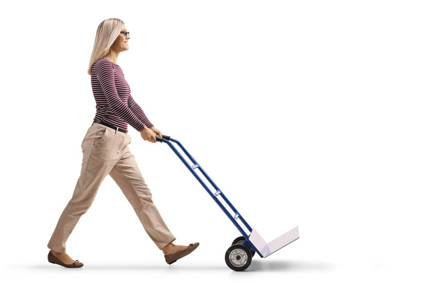 Full length profile shot of a young woman pushing an empty hand-truck isolated on white background - Фото, зображення