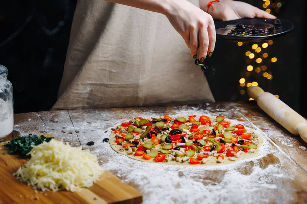 Home Made Pizza Cooking. Woman hand cook pouring olives slices on dough. Food preparing concept under quarantine due to epidemic. - Фото, зображення
