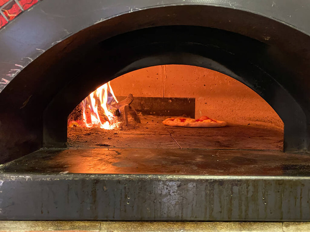 Bakoven, open haard in het midden naast rijzende deegpizza, Italiaanse traditionele schotel - Foto, afbeelding