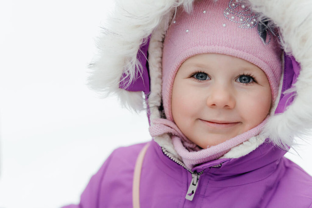 雪の背景に通りにピンクのキャップに小さな笑顔の少女の肖像画。高品質の写真 - 写真・画像
