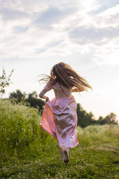girl running across the field in a pink dress - Foto, afbeelding