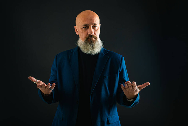 Smiling business man with beard showing man, gesturing with hands, showing something, isolated on dark background. Low key. The portrait is emotional - Photo, Image