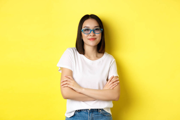 ファッションとライフスタイルのコンセプト。セクシーなと自信に満ちたアジアの女性で流行のサングラス見て自己保証でカメラ,上に黄色の背景 - 写真・画像