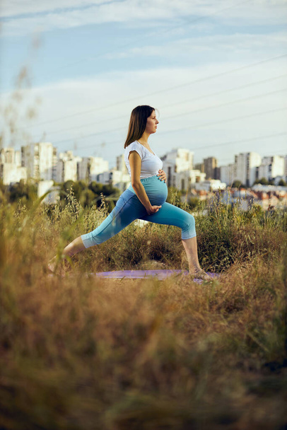 Hilal yoga pozuyla çayırda duran hamile bir kadın.. - Fotoğraf, Görsel