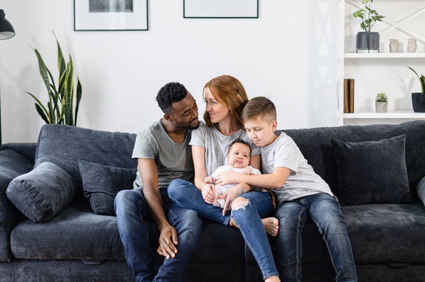 A multiracial family sits on the couch at home - Fotoğraf, Görsel