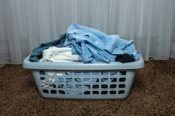 Сірий пластиковий кошик з брудною білизною в спальні на килимі
 - Фото, зображення