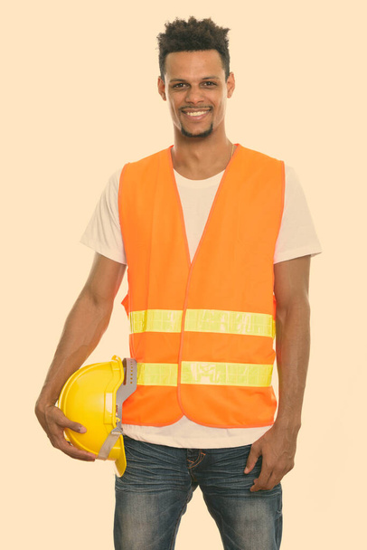 Joven feliz africano trabajador de la construcción sonriendo mientras sostiene el casco de seguridad - Foto, Imagen