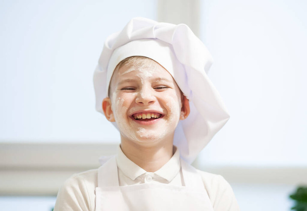 Little cute boy dressed as a cook  in the kitchen - Fotó, kép