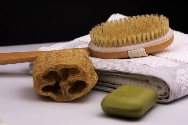 Close-up of a brush, a green soap bar, a loofah and a white towel, with black background and copy space - Fotoğraf, Görsel