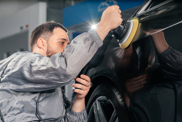 Worker polishing car with special grinder and wax from scratches at the car service station. Professional car detailing and maintenance concept - Photo, Image