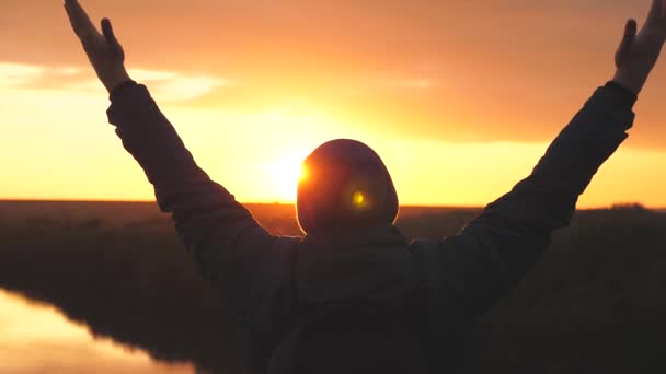 Silhouet van een man bij zonsondergang met opgeheven handen tegen de zonsondergang. Een man droomt van zweven in de lucht met open armen. Droom en bid kijkend naar de hemel - Video