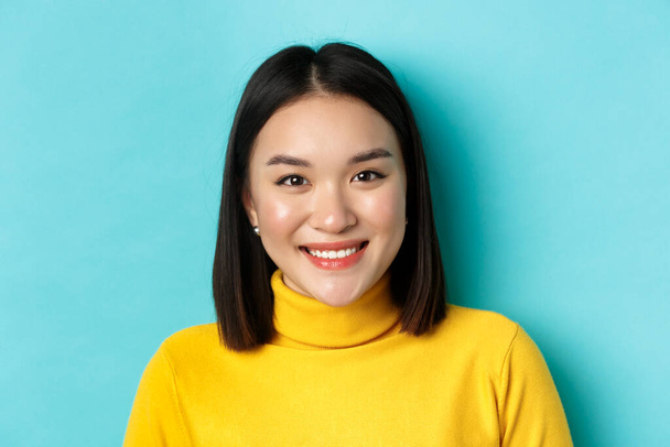 Szépség és bőr koncepció. Közelkép mosolygós ázsiai női modell tökéletes bőr és fehér fogak, álló felett kék háttér - Fotó, kép