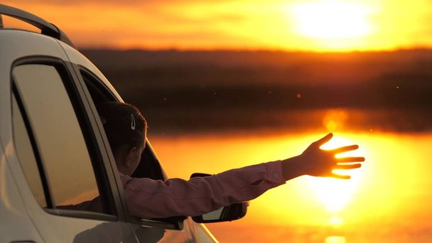 La conductora se detuvo en el camping en coche, mirando a la puesta de sol. Una viajera libre agitando los brazos desde su coche disfrutando de la vista del amanecer sobre el lago y admirando el hermoso paisaje. - Foto, imagen