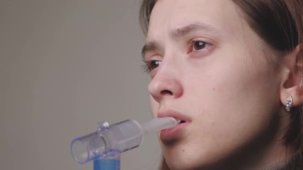 A menina respira em uma solução da inalação de pulmões. Uma jovem em quarentena trata uma tosse inalando vapor com remédios. Tratamento de uma pessoa em casa com equipamento profissional para resfriados - Filmagem, Vídeo