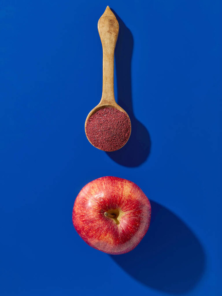 Dřevěná lžíce ovocného prášku a čerstvého jablka na modrém pozadí, horní pohled - Fotografie, Obrázek