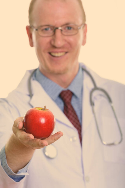 Studio shot of happy man doctor smiling while giving red apple with focus on apple - Photo, Image