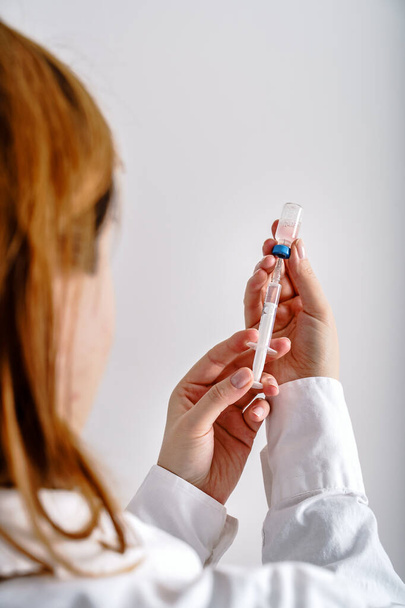 Close up on hand of unknown caucasian woman doctor holding syringe with needle and vaccine injection in front of white wall - covid-19 coronavirus vaccination concept healthcare and medicine - Photo, Image