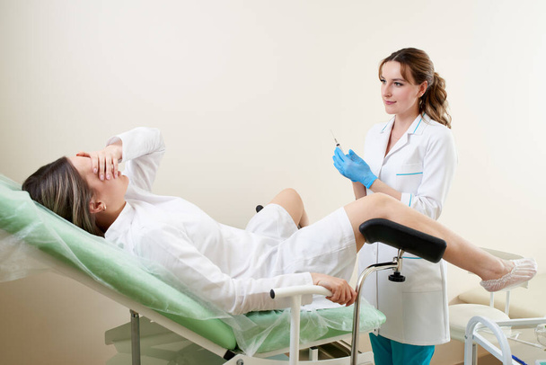 Jinekolog jinekoloji kürsüsünde oturan bir hastayı muayene ediyor. - Fotoğraf, Görsel