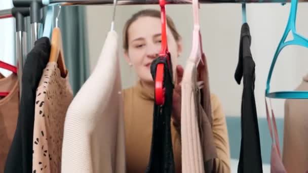 Nuori nainen kävelee takana pitkä teline vaatteita hänen vaatekaappi makuuhuoneessa - Materiaali, video