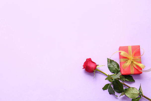 Mooie rode roos en cadeau op kleur achtergrond - Foto, afbeelding