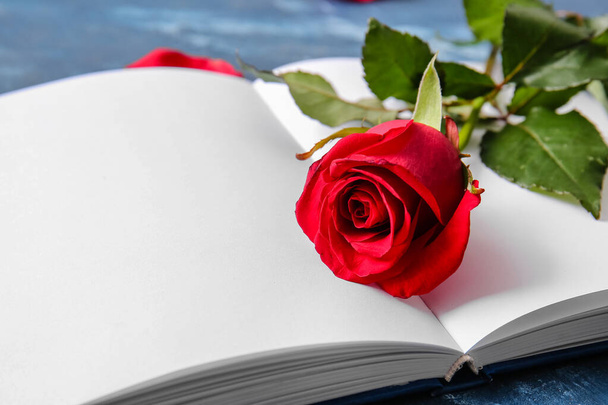 Boek met blanco pagina 's en mooie rode roos op kleur achtergrond, closeup - Foto, afbeelding