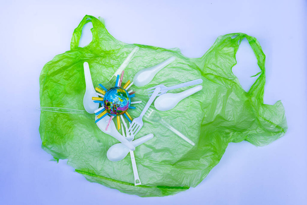 Πλαστικά προϊόντα, όπως πλαστικές σακούλες, λευκά και διάφανα πλαστικά κουτάλια, τοποθετήθηκαν σε λευκό φόντο. Globe αντιπροσωπεύει πλαστικό υλικό που γεμίζει τον πλανήτη μας και μολύνει τη φύση. - Φωτογραφία, εικόνα
