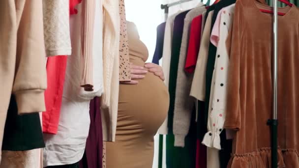 Těhotná mladá žena s velkým břichem chůze ve velkém šatníku a hledají oblečení na sebe - Záběry, video