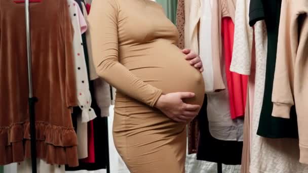 Szekrény a terhes fiatal nő nagy hasa a nagy bevásárlóközpont hosszú állványok lógó ruhák terhes nő - Felvétel, videó