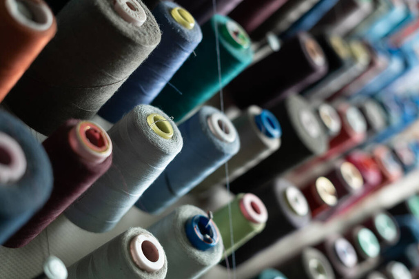 Sewing threads of different colors are installed on a metal wall and are in the sewing workshop. Manufacturing and material diversity concept. Copy space. - Photo, Image