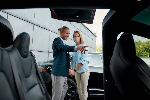 Smiling young caucasian businessman pointing into car interior - Foto, Imagem