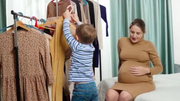 Pieni lapsi poika auttaa äitiään valitsemalla vaatteita pukeutua vaatekaappi makuuhuoneessa. - Materiaali, video