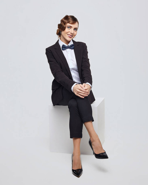 attractive woman with a retro hairstyle poses in a man's suit. photo shoot in the studio on a white background - 写真・画像