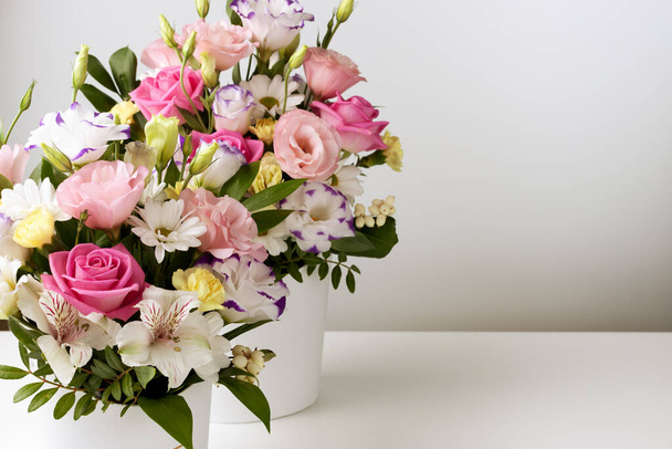 mock up two bouquets of different sizes of roses, daisies, lisianthus, chrysanthemums, unopened buds in a white paper box on a white table and wall - Photo, Image