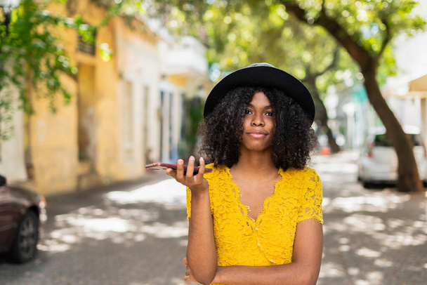 young black woman with curly hair, with red mask, yellow dress, using her smart phone - Foto, immagini