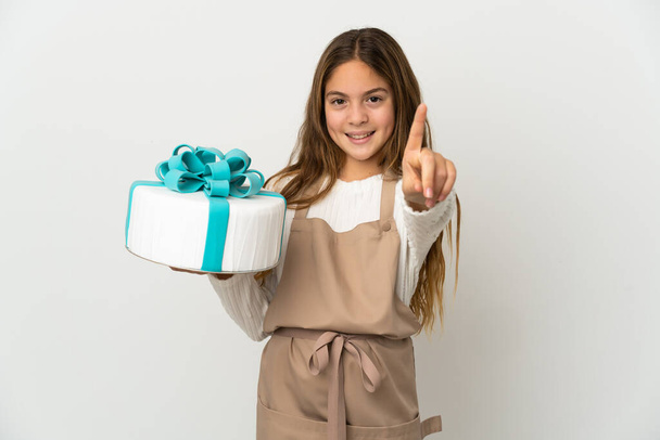 Klein meisje met een grote taart over geïsoleerde witte achtergrond tonen en tillen van een vinger - Foto, afbeelding